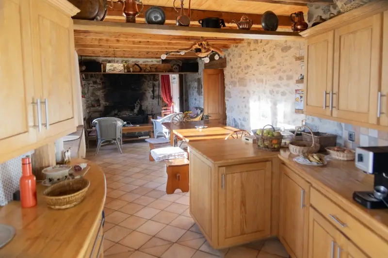 Cuisine en bois ouverte sur la salle à manger et la grande cheminée en pierre